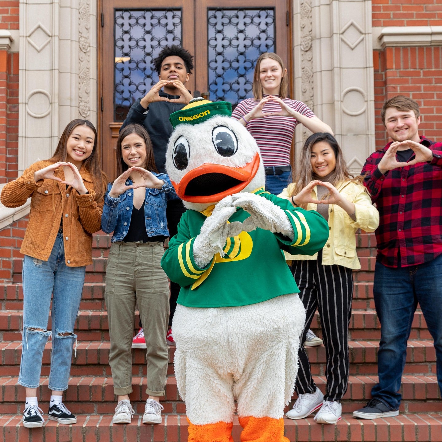 Undergraduate students and the UO Duck making the O symbol with their hands