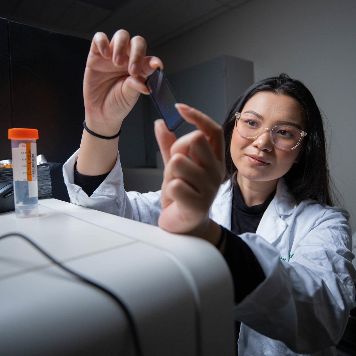 A person in a lab coat looking at a microscope slide